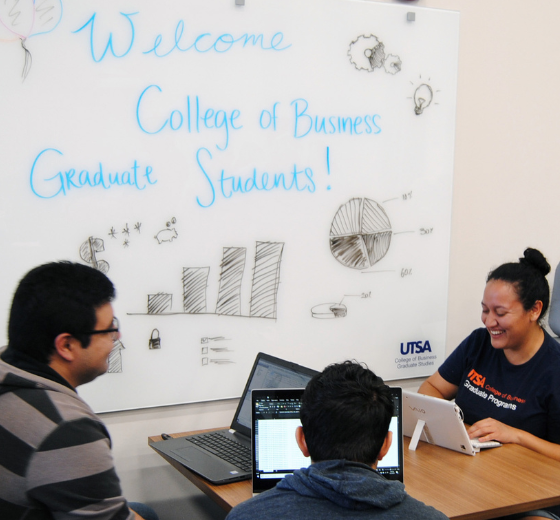 Image of three students studying at a table with a white board in the background,