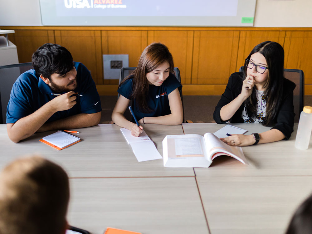 students at a table looking at a book and taking notes