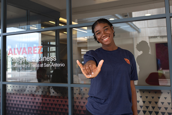 Female student making Birds Up hand gesture in front of a logo for the Carlos Alvarez College of Business