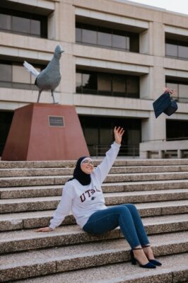 Farah Hamed in front of roadrunner monument throwing graduation cap