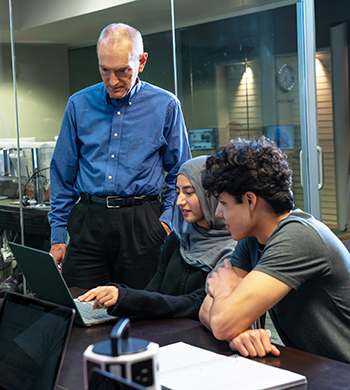 Man working with students in front of a computer screen.